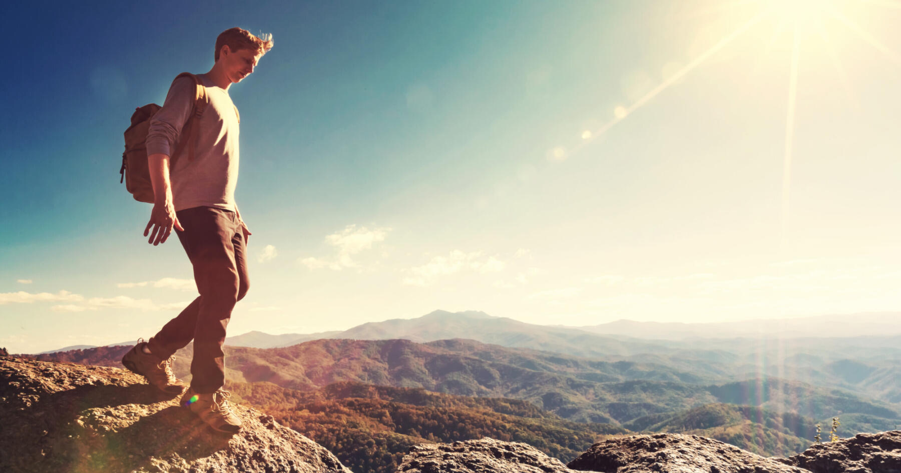 Man walking on the edge of a cliff high above the mountains SBI 317640385