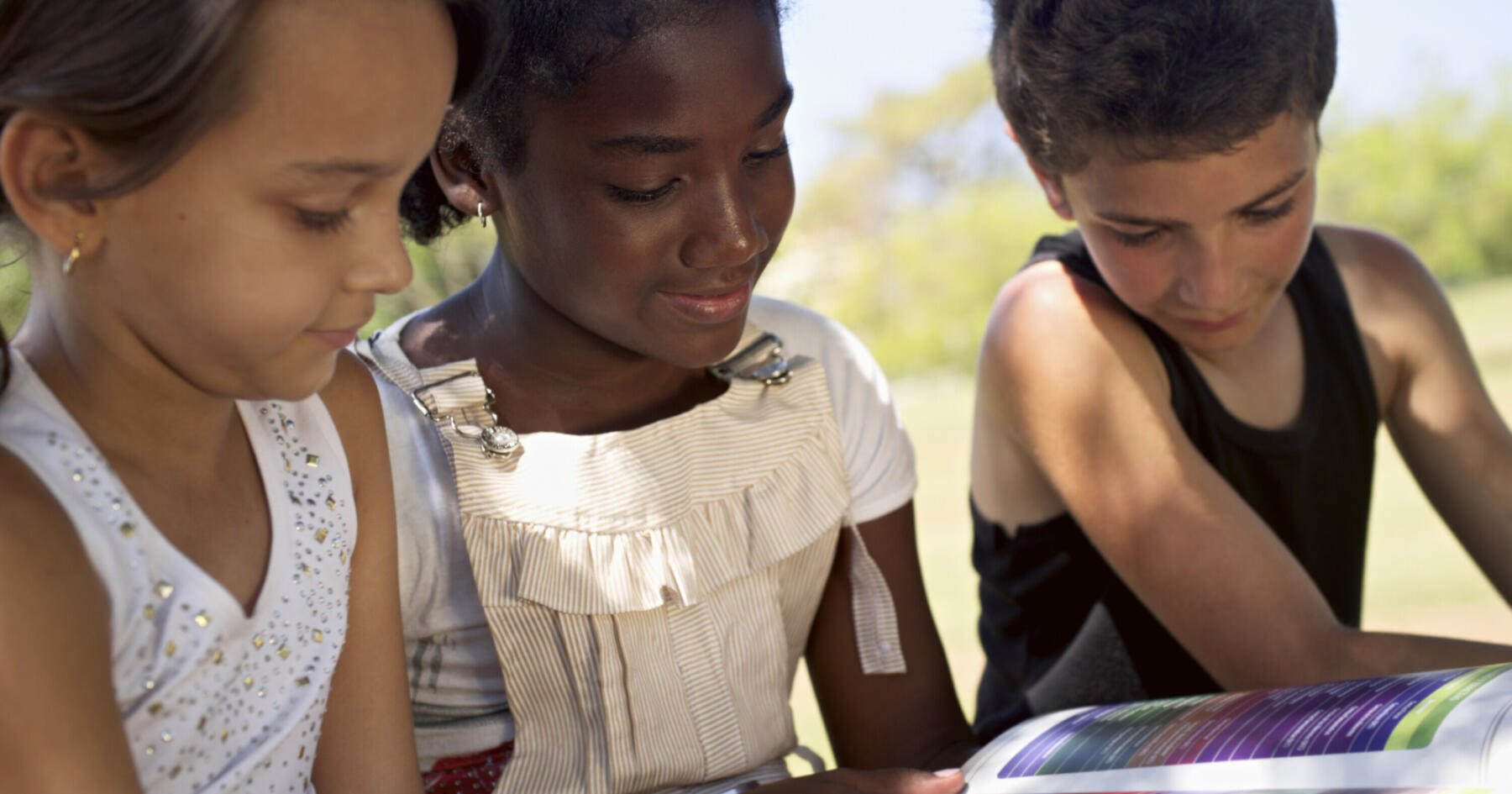 Young people and education two little girls and one boy reading book in city park SBI 310153650